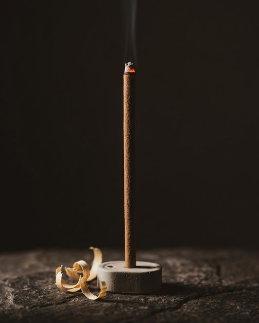 Close-up of a glowing Chandan Tattva dhoop stick tip with a thread of smoke, beside sandalwood