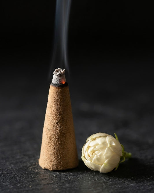 Close-up of a glowing Mogra Dhyaan dhoop cone beside mogra flowers, a thread of smoke rising