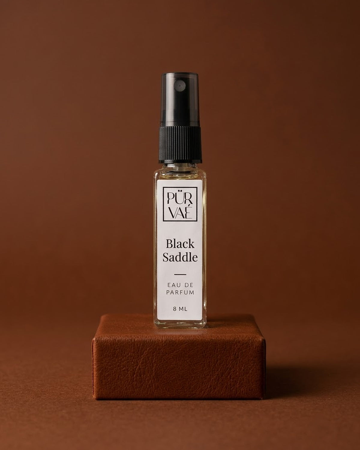 Black Saddle eau de parfum 8 ml glass spray on a cognac leather plinth
