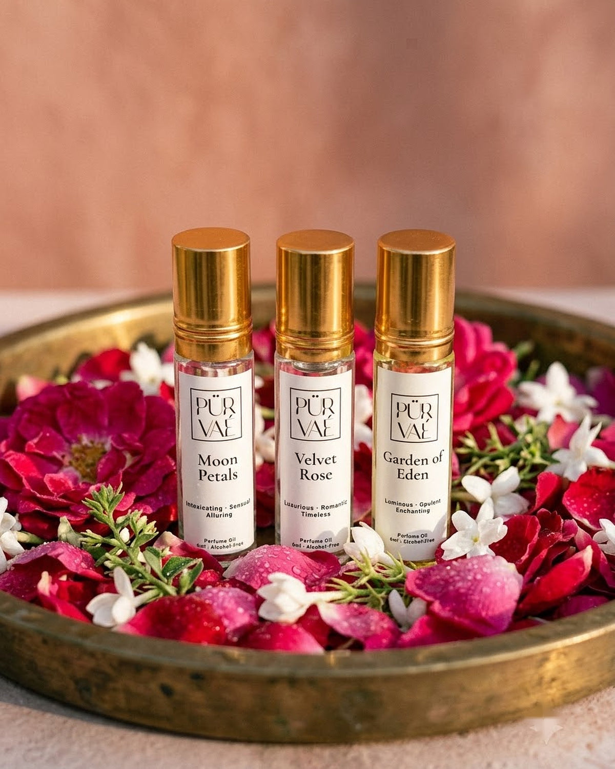 Purvae Bloom Trio: Moon Petals, Velvet Rose and Garden of Eden 6 ml parfum oil roll-ons in a brass tray of rose petals and jasmine