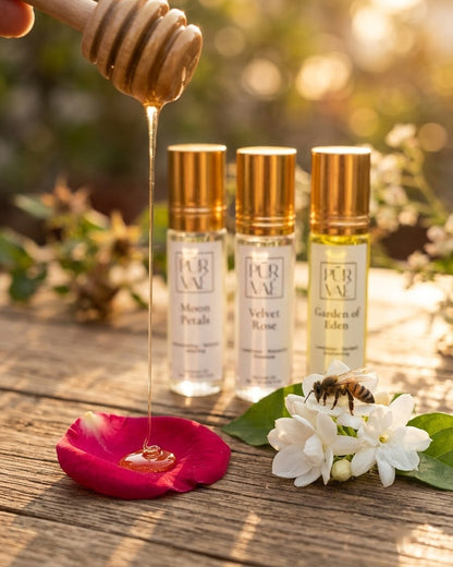Honey from a wooden dipper falling onto a rose petal beside the three Bloom Trio parfum oils and a bee on jasmine