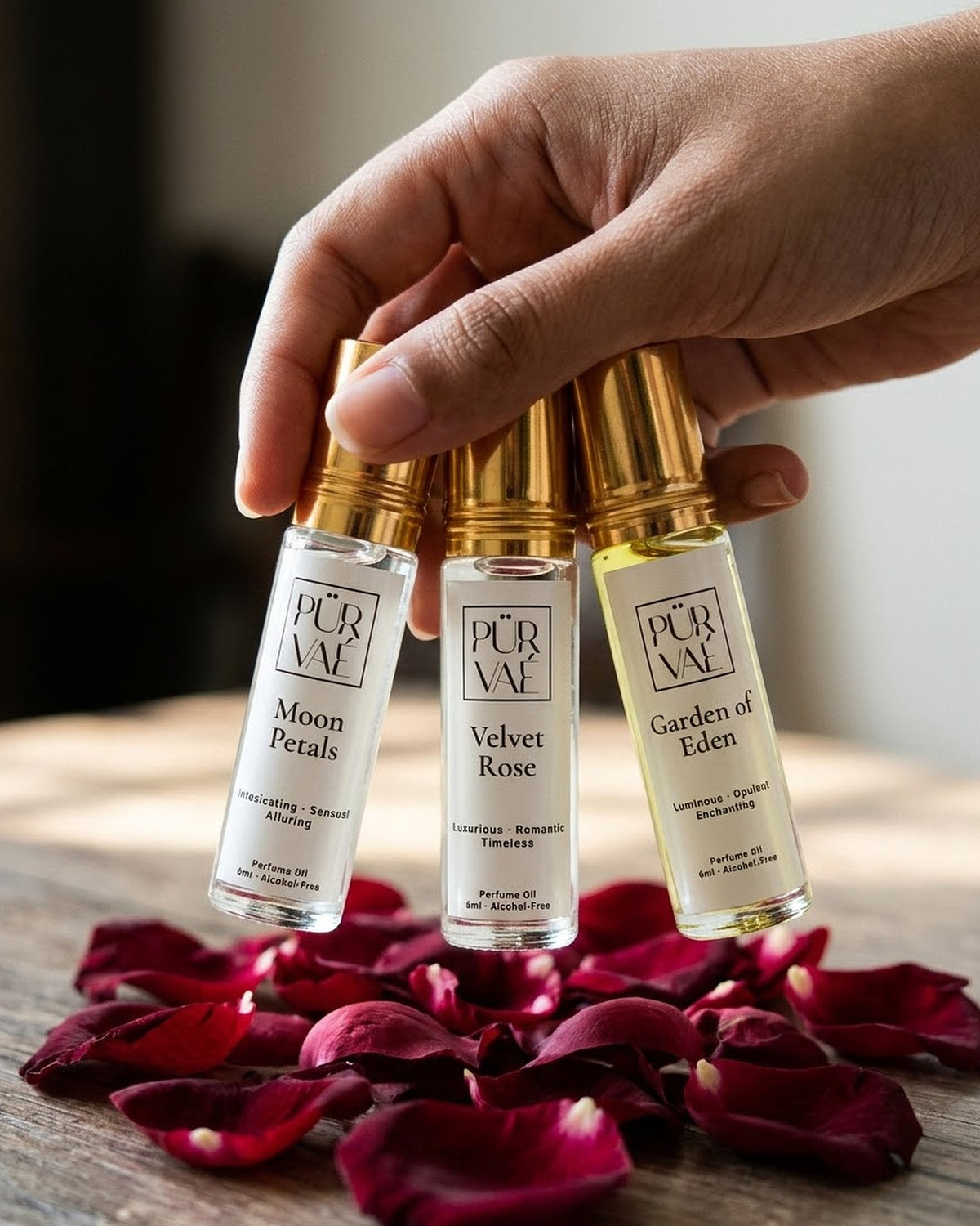 A hand holding the three 6 ml Bloom Trio roll-ons above scattered rose petals to show their size