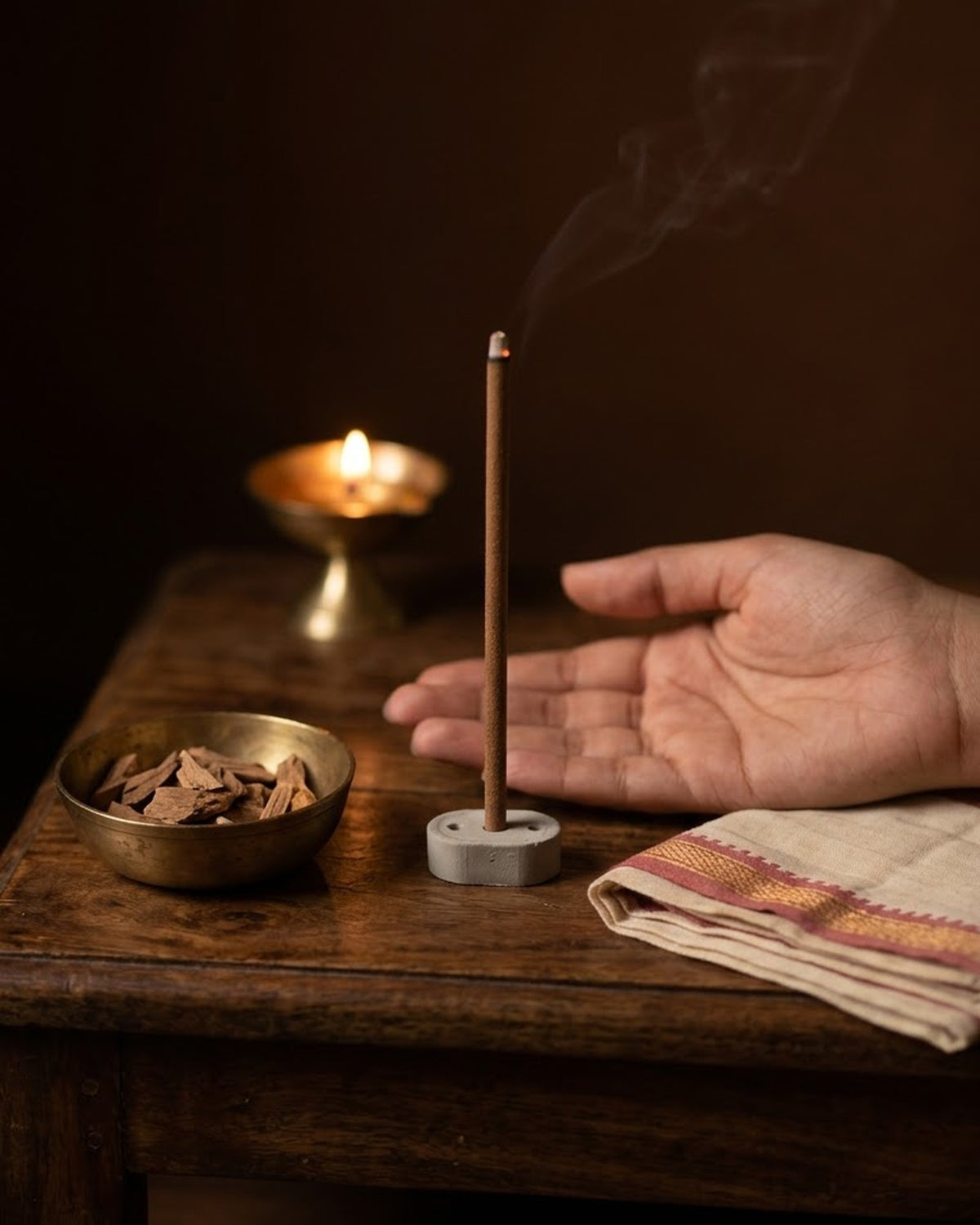 Chandan Tattva dhoop stick burning at a puja corner with a brass diya and a split sandalwood log