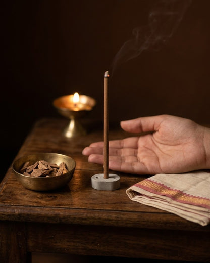 Chandan Tattva dhoop stick burning at a puja corner with a brass diya and a split sandalwood log