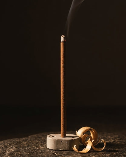 Glowing Chandan Tattva dhoop stick in its holder with smoke rising, beside sandalwood