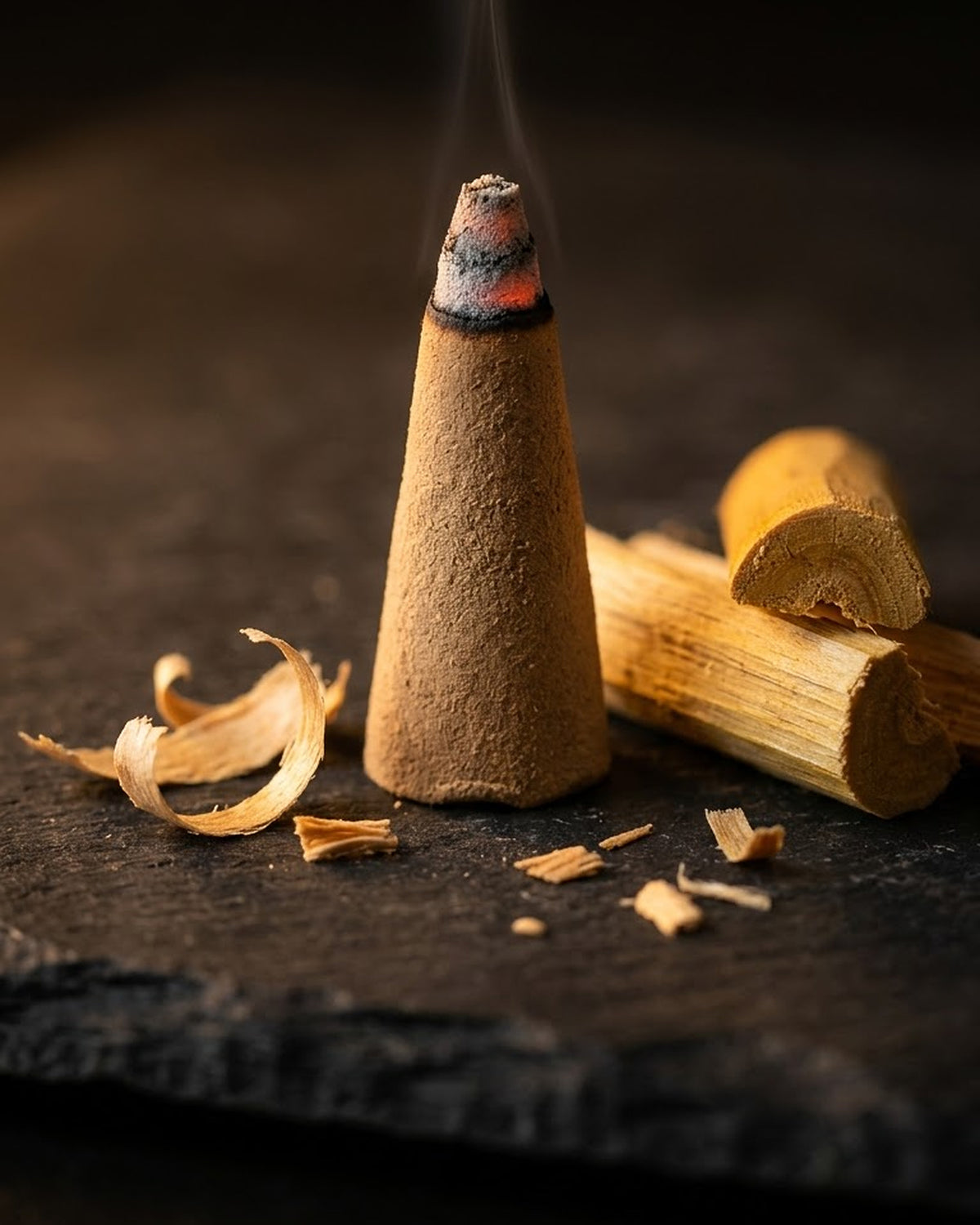 Close-up of a glowing Chandan Vritti dhoop cone beside sandalwood, a thread of smoke rising