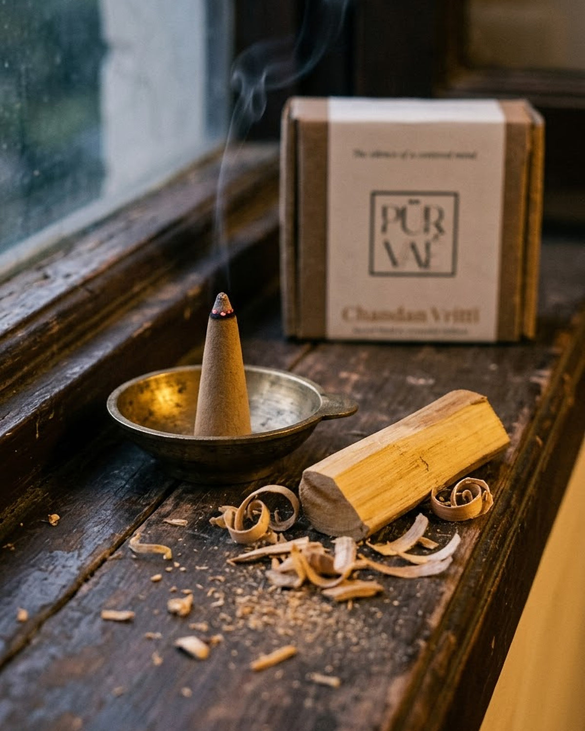 Chandan Vritti dhoop cone smouldering on a wooden ledge by a window, with sandalwood
