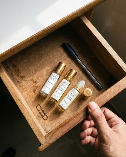 The three 6 ml Day Trio roll-ons lying in an open wooden desk drawer beside a pen and paperclip to show their size