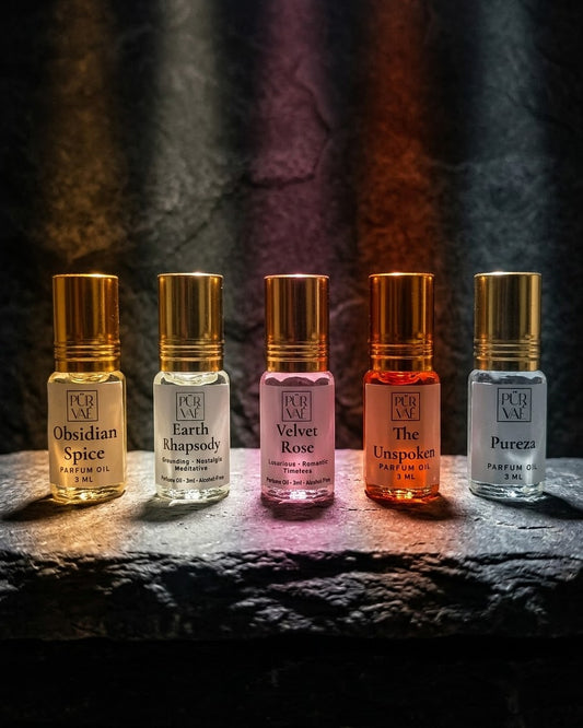 Purvae Discovery Five: five 3 ml parfum oil roll-ons (Obsidian Spice, Earth Rhapsody, Velvet Rose, The Unspoken, Pureza) standing in a row on a dark stone shelf, each in its own coloured light