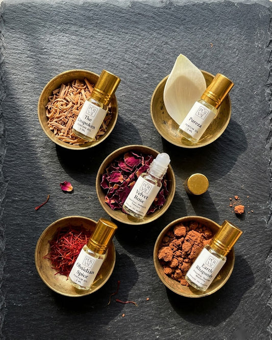 Five 3 ml Purvae parfum oil roll-ons resting in brass katoris with sandalwood, lotus petal, rose petals, saffron and red earth