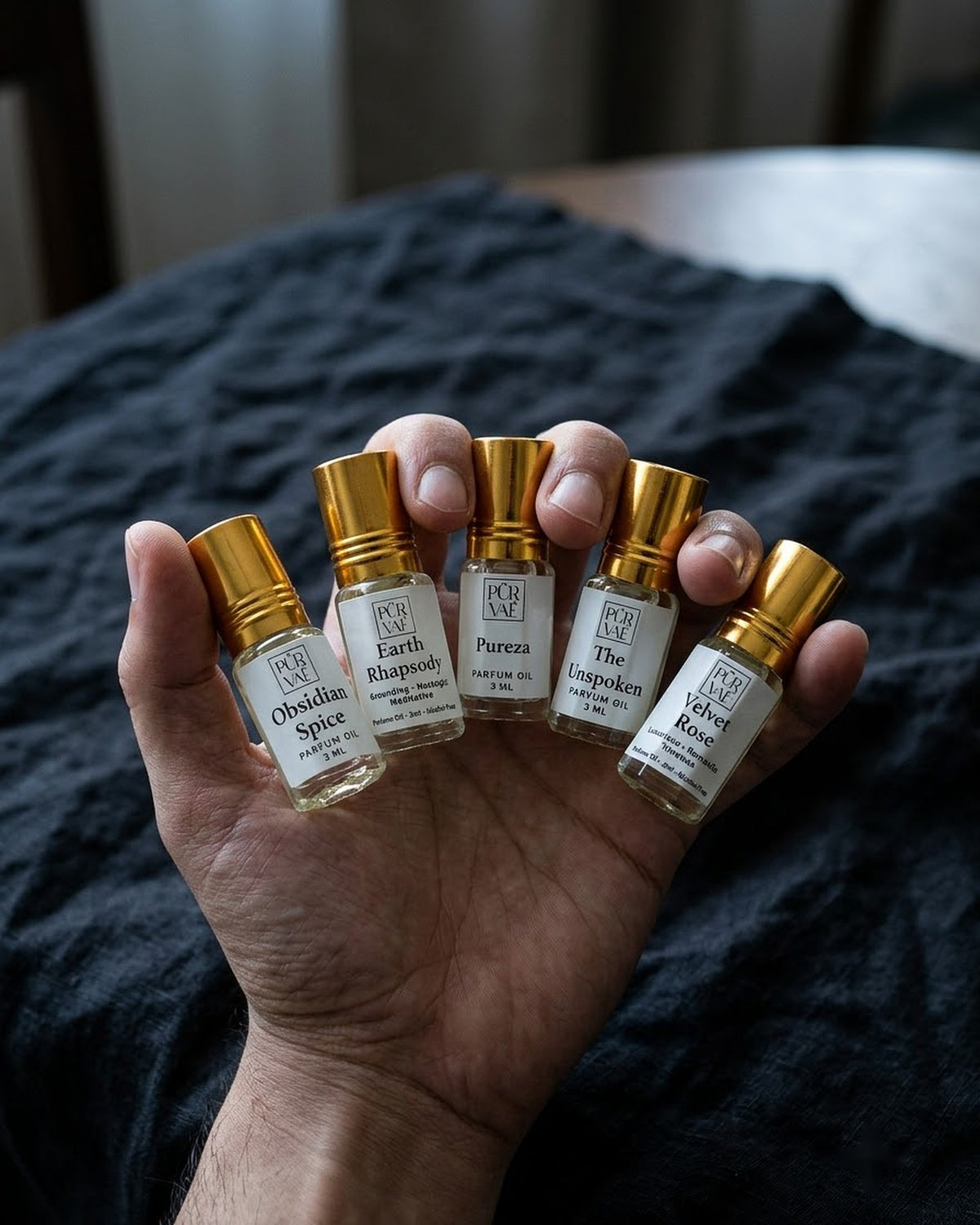 A hand fanning all five Purvae 3 ml parfum oil roll-ons between the fingers to show their small size