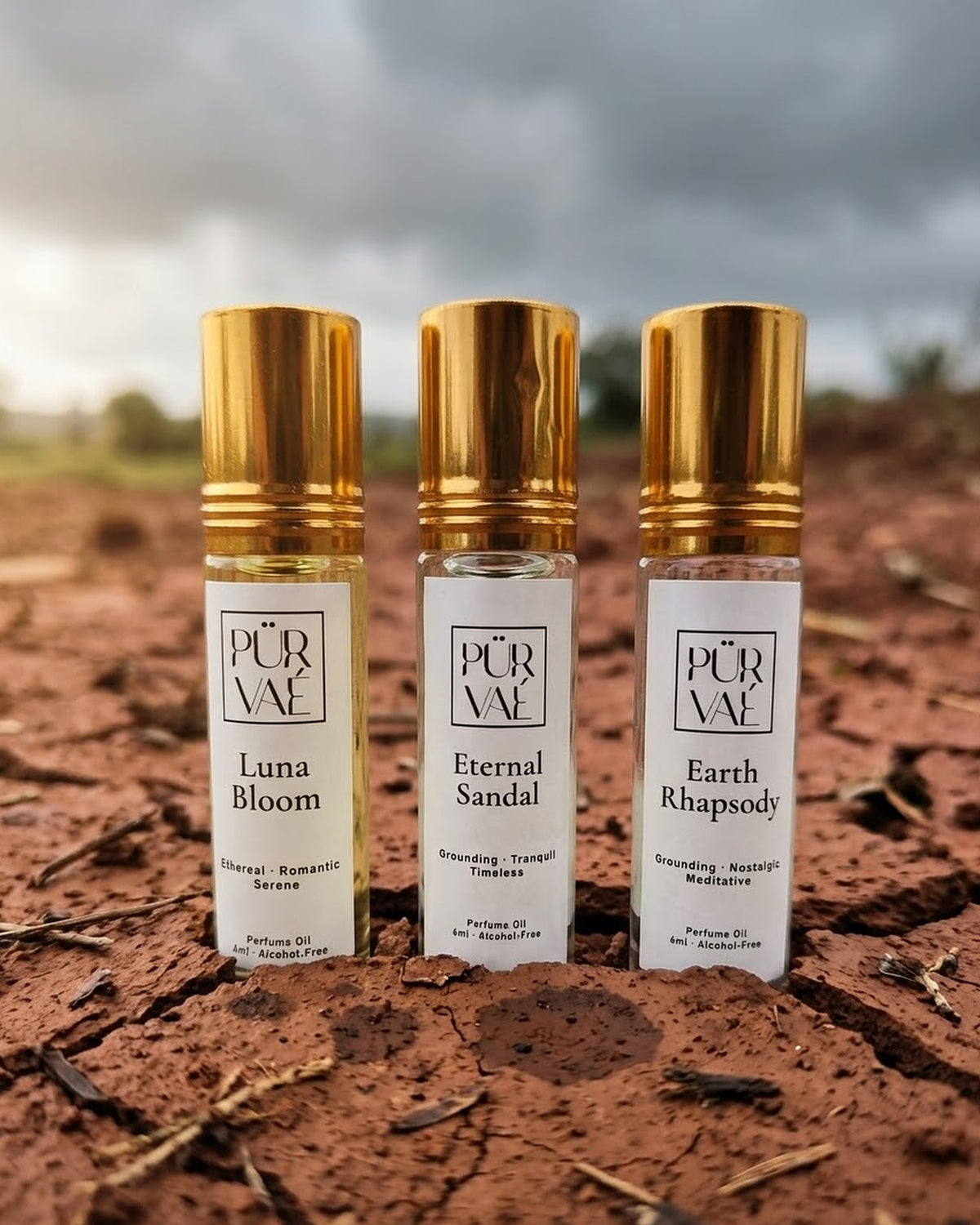 Purvae Earth Trio: Luna Bloom, Eternal Sandal and Earth Rhapsody 6 ml parfum oil roll-ons standing in cracked red earth under a monsoon sky