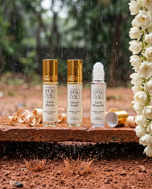 Earth Trio parfum oils on a clay ledge in the rain with sandalwood shavings and a jasmine garland, raindrops splashing red earth