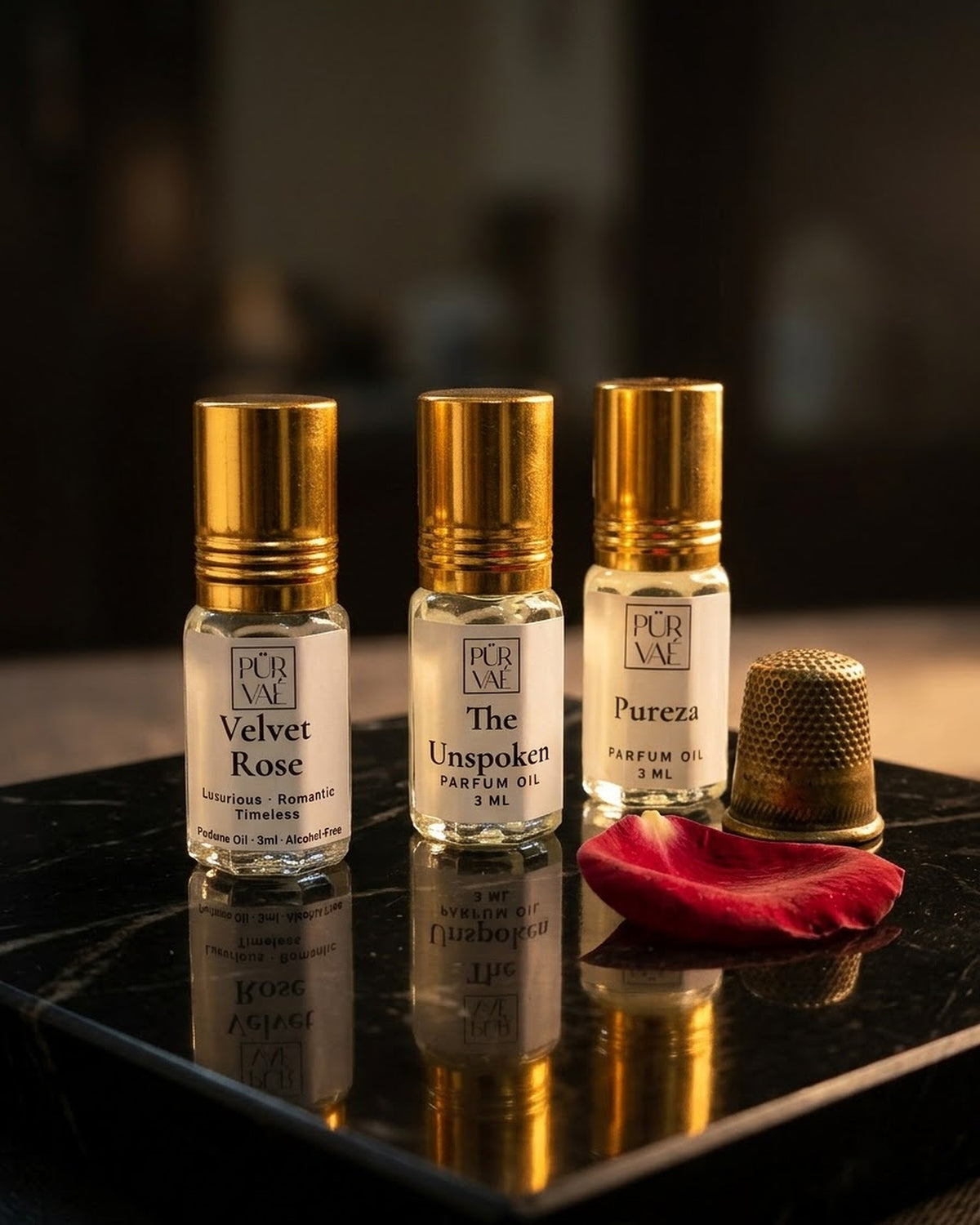 Purvae First Trio: Velvet Rose, The Unspoken and Pureza 3 ml parfum oil roll-ons on a black marble square with a rose petal