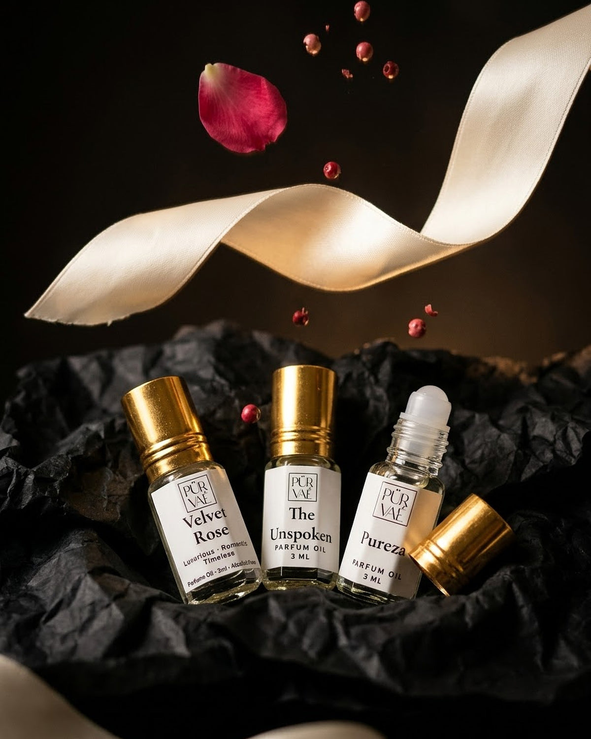 First Trio 3 ml parfum oils lying in black tissue under a floating ivory silk ribbon and rose petal