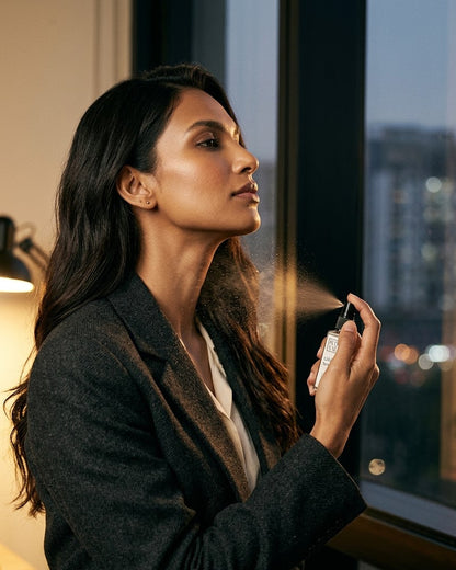 Woman in a charcoal blazer spraying Gilded Smoke on her neck