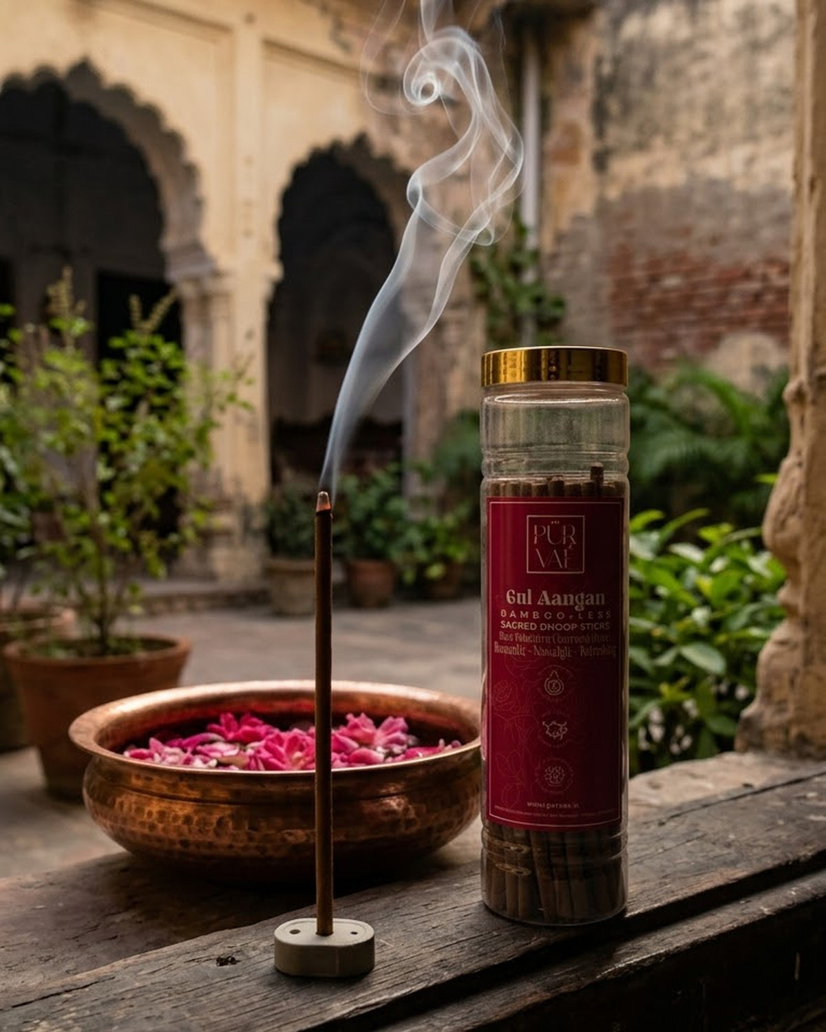 Gul Aangan dhoop stick burning in an old courtyard beside a copper urli of rose petals, Purvae jar nearby