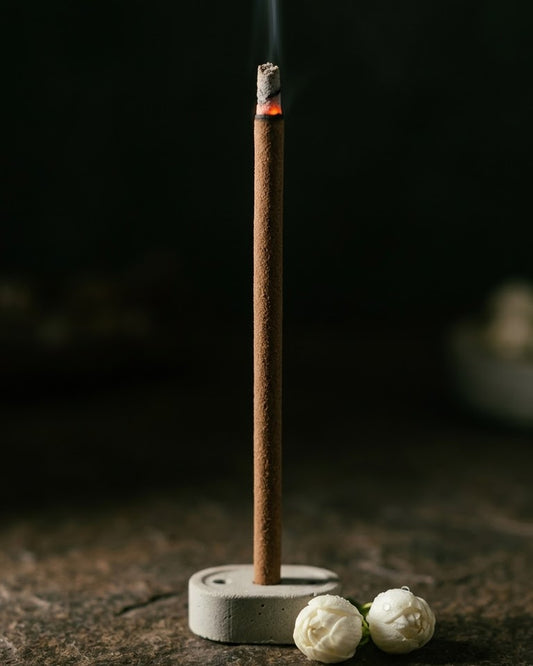 Close-up of a glowing Mogra Saanjh dhoop stick tip with a thread of smoke, beside mogra flowers