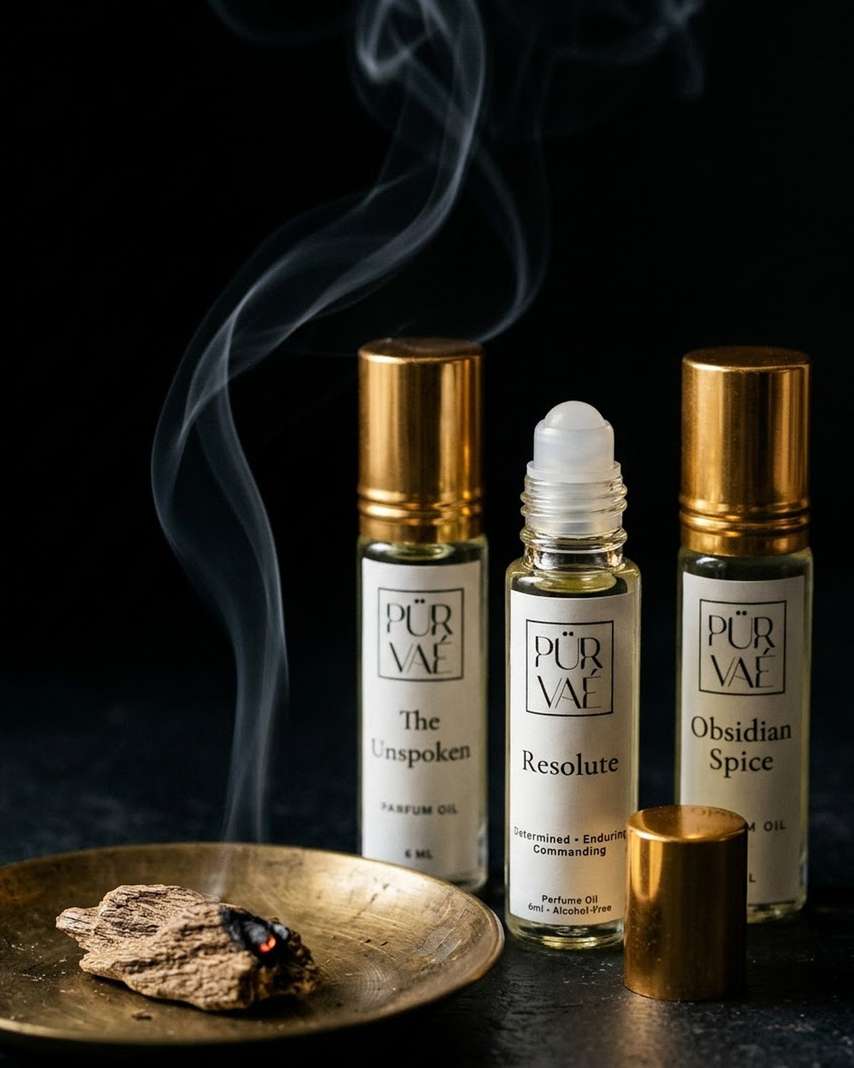 Night Trio parfum oils beside a smouldering oud chip on a brass dish, with the Resolute roller ball showing