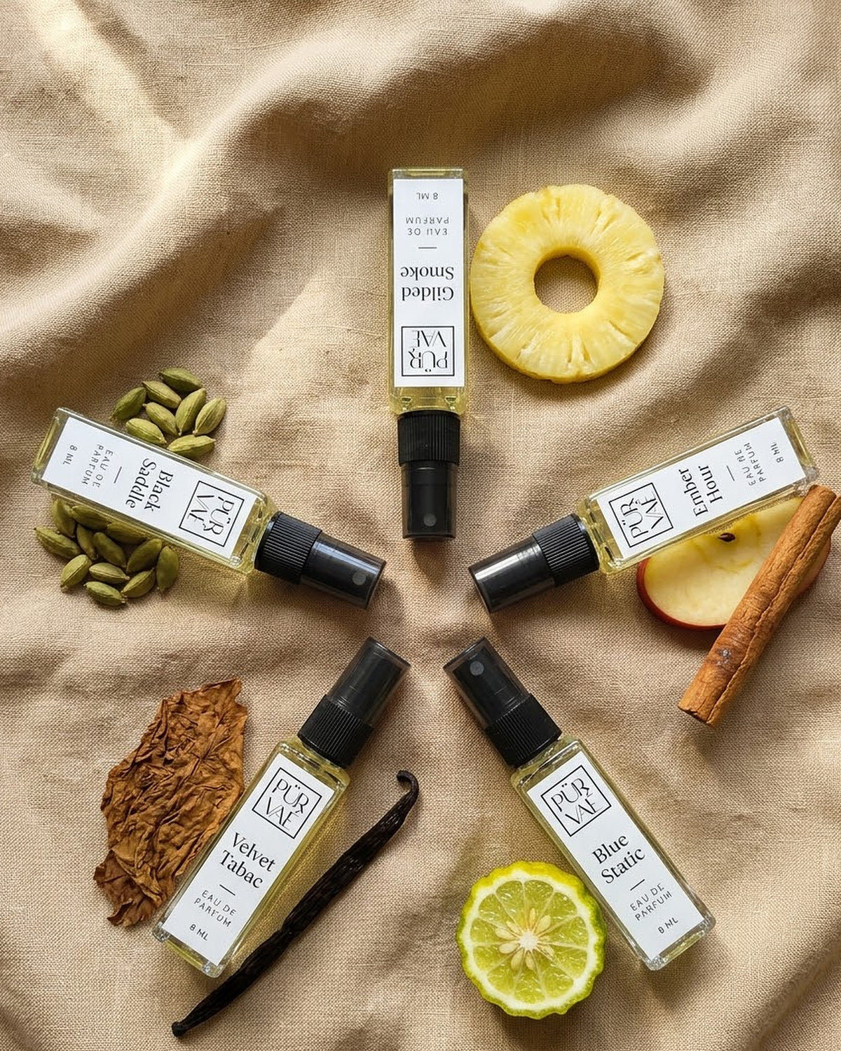 Flat lay of the five bottles with cardamom, pineapple, apple, bergamot and tobacco leaf